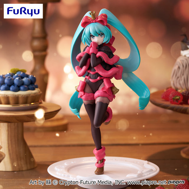 Colorful figurine with blue hair and pink outfit on a decorative stand with blurred dessert background